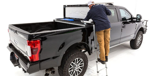 Wide shot of a man standing on the DECKED Truck Tool Box ladder putting tools in his truck